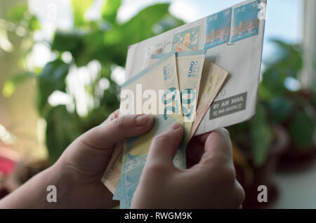 In Frauenhand einen Umschlag mit Briefmarken von Hong Kong und Euro-banknoten Stockfoto