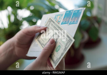 In Frauenhand einen Umschlag mit Briefmarken von Hong Kong und Dollar Banknote Stockfoto
