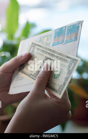 In Frauenhand einen Umschlag mit Briefmarken von Hong Kong und Dollar Banknote Stockfoto