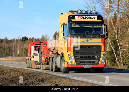 Salo, Finnland - 1. März 2019: Gelb Volvo FH Truck von Silvasti hols Sandvik LH 209 L U-Lader oder LHD am Anhänger auf der Autobahn am Tag der Feder Stockfoto