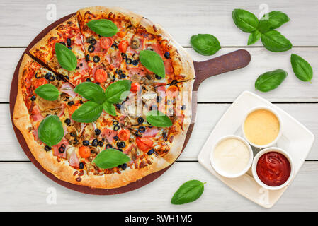 Blick von oben auf eine traditionelle italienische Pizza mit Schinken, Pilzen, Tomaten, Mozzarella, schwarze Oliven mit Basilikum und Saucen dekoriert Stockfoto