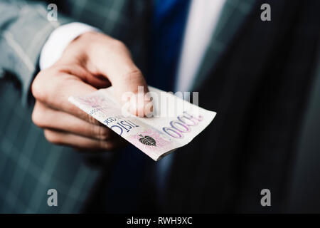 Nahaufnahme eines jungen kaukasischen Geschäftsmann, tragen einen eleganten grauen Anzug, eine 1000 Tschechische Kronen Banknote der Beobachter Stockfoto