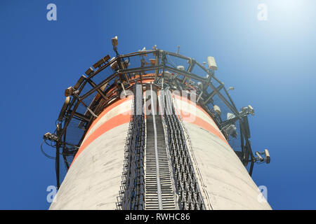 Hohe industrielle konkrete Schornstein Turm mit einem zellulären Telekommunikation Mobilfunk Antennen auf die Oberseite mit Kabel mit blauem Himmel und sunray angeschlossen Stockfoto