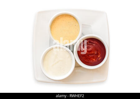 Blick von oben auf die drei Soßen in Schalen auf einem Teller auf weißem Hintergrund mit Senf, Ketchup und Mayonnaise isoliert. Stockfoto