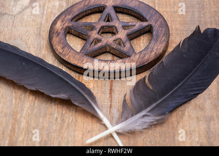 Zwei Black Raven Federn und Holz umgeben Pentagramm Symbol auf Holz Hintergrund. Fünf Elemente: Erde, Wasser, Luft, Feuer, Geist. Stockfoto