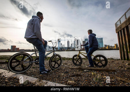 Zwei Männer auf BMX Fahrräder in Greenwich Halbinsel mit Blick auf Canary Wharf Financial District über die Themse, London, England, Vereinigtes Königreich Stockfoto