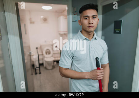Portrait einer jungen, männlichen Reiniger bei der Arbeit. Er hält einen Mop. Stockfoto
