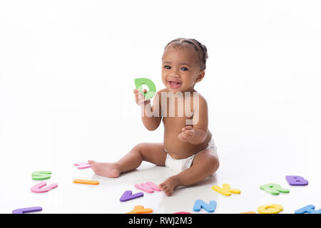 Ein lächelndes sechs Monate alten Baby Mädchen mit einem weißen Windel. Sie sitzt auf einem weißen nahtlose Hintergrund und spielen mit Schaum alphabet Spielzeug. Stockfoto