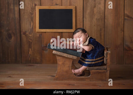 Eine Woche alt neugeborenes Mädchen trägt ein Kleid und das Schlafen auf einem Stapel von Vintage Bücher bei einer kleinen Schule Schreibtisch. Stockfoto