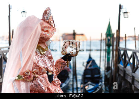 Venezianische Masken Modell aus der Karneval von Venedig 2019 mit Gondeln im Hintergrund Stockfoto