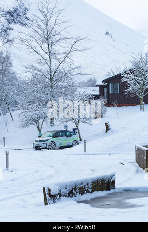 BMW-Elektroauto an elektrischen Auto aufgeladen Ladestation Punkt in verschneiten Parkplatz durch Clachaig Inn, Glencoe, Highlands, Schottland im Winter Stockfoto