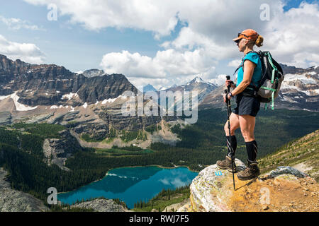 Weibliche Wanderer auf der Klippe mit Blick auf die Berge und das Tal mit bunten Alpine Lake, British Columbia, Kanada Stockfoto