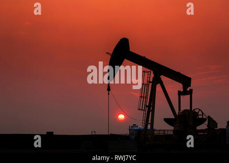 Silhouette von pumpjack mit einem leuchtenden warmen Sonne Ball im Hintergrund, westlich von Airdrie; Alberta, Kanada Stockfoto