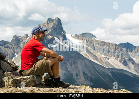 Männliche Wanderer sitzen auf einem Felsen mit Blick auf die Berge Vista im Hintergrund; British Columbia, Kanada Stockfoto