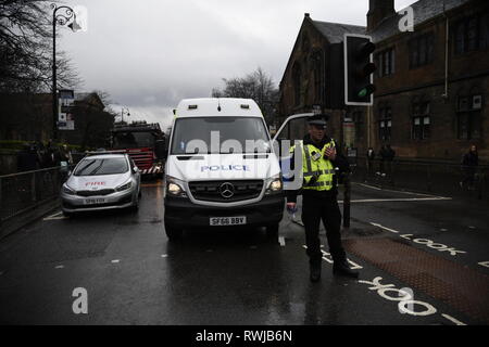 Glasgow, Glasgow, UK. 6 Mär, 2019. Ein Polizist wird beobachtet, als er im Radio auf dem Gebiet der Szene. Polizei ein verdächtiges Paket an der Universität Glasgow in Schottland gefunden haben. Polizei und Campus Mitarbeiter haben den Bereich abgeschaltet. Credit: Stewart Kirby/SOPA Images/ZUMA Draht/Alamy leben Nachrichten Stockfoto