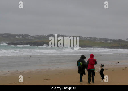 County Donegal, Irland. 06. März 2019. Irland Wetter - nach schweren nächtlichen Regen war es ein Tag der starken Winde und Regen in County Donegal. Frauen spielen mit Hund auf nassen und windigen Tag auf Dunfanaghy Beach. Quelle: David Hunter/Alamy Leben Nachrichten. Stockfoto