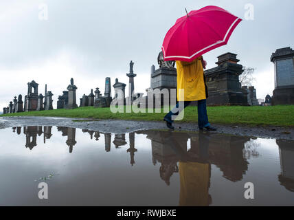 Glasgow, UK. 6 Mär, 2019. Schwere und lang anhaltenden Regen in Glasgow hat dieses hell gekleidete Frau nicht vom Besuch der berühmten nekropole Friedhof im Osten der Stadt abhalten. Credit: Iain Masterton/Alamy leben Nachrichten Stockfoto