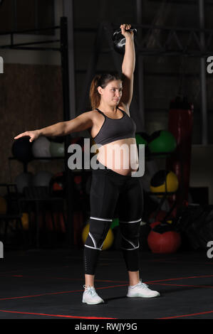 Schwangere weiblichen Athleten dabei hängen kettlebell sauber und drücken Sie Stockfoto