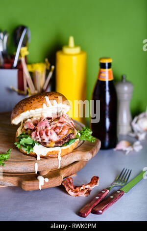 Bacon Burger mit Aioli Sauce auf einem Holzbrett, aus der Nähe. Hamburger fast food Zutaten. Stockfoto