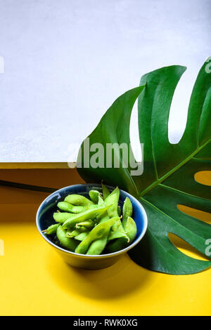 Edamame gedämpfte Bohnen, Sojabohnen mit Salz bestreut in der Systemgruppe. Japanische Snack, asiatische Küche. Grauen und gelben Hintergrund. Stockfoto