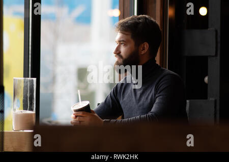 Schöne nachdenkliche bärtigen Kerl in der Nähe der Fenster in einem Café. attraktive junge stilvollen Mann in einem Cafe sitzen und schauen aus dem Fenster. Unternehmen, freiberuflich Stockfoto