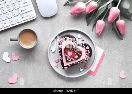 Valentine Herz Kuchen mit Text "Happy Valentine". Ansicht von oben auf die Tabelle mit der Tastatur, der Maus, einige Karten und Tulpen. Stockfoto