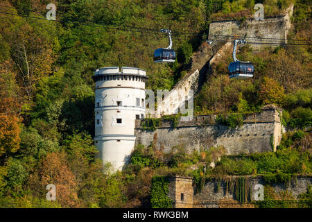 Weißer runder Turm auf treed Hügel mit alten Steinmauer und Gondeln entlang der Kabel; Koblenz, Deutschland Stockfoto