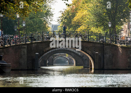 Mehrere steinerne Brücke arch Möglichkeiten an einem Kanal mit mehreren Fahrrädern auf Geländer; Amsterdam, Niederlande Stockfoto