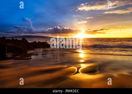 Einen goldenen Sonnenuntergang mit Reflexion auf Sand auf einem leeren Strand; Makena, Maui, Hawaii, Vereinigte Staaten von Amerika Stockfoto