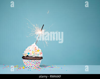 Cupcake mit Streuseln und eine Wunderkerze über einen blauen Hintergrund. Stockfoto