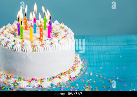 Weiß Buttercream Vereisung Geburtstag Kuchen mit mit bunten Streuseln und Kerzen über blauer Hintergrund Stockfoto