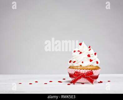 Vanilla Cupcake mit buttercream Vereisung, herzförmige besprüht und eine rote Schleife. Stockfoto