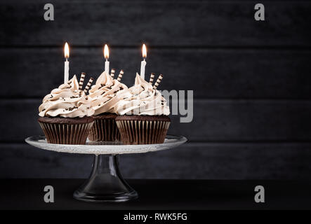 Drei chocolate buttercream Cupcakes mit Zuckerglasur und Geburtstag Kerzen auf der Torte stand Stockfoto