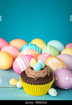 Bunte Ostereier und Cupcake mit Nest auf einem blauen Hintergrund. Stockfoto