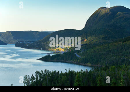 Auf der Südseite von Bonne Bay und am Fuß des Mount Krähe ist die Stadt der Shoal Bach durch einen kleinen Punkt des frühen Morgens das Sonnenlicht beleuchtet, Gros Morne National Park, Neufundland, Kanada Stockfoto