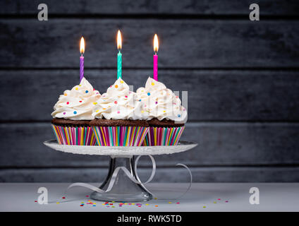 Drei chocolate buttercream Cupcakes mit Zuckerglasur und Geburtstag Kerzen auf der Torte stand Stockfoto