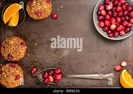 Frisch gebackene cranberry Muffins auf einem urigen Backblech mit Preiselbeeren und Orangenscheiben. Stockfoto