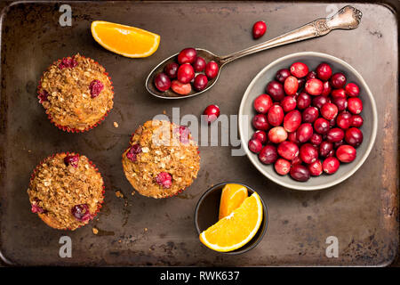 Frisch gebackene cranberry Muffins auf einem urigen Backblech mit Preiselbeeren und Orangenscheiben. Stockfoto