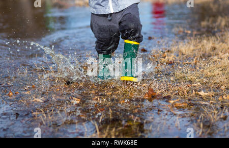 Sehr nass kleiner Junge läuft durch Pfützen im Gras rainboots tragen. Stockfoto