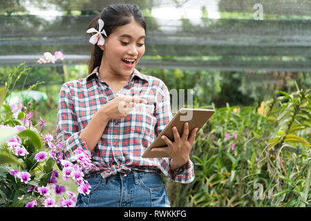 Weibliche Gärtner tragen Karohemden. Es gab Orchideen herauf die Ohren, die Hand mit der Tablette und Pointing Finger auf dem Tablett und lächelnd Stockfoto