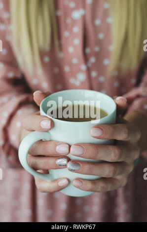 Weibliche Hände halten eine weiße Tasse mit Getränk. Close Up. Unscharfer Hintergrund Stockfoto