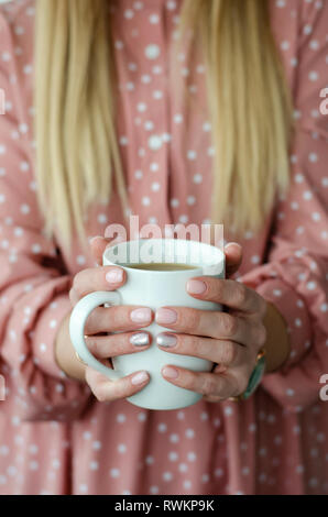 Weibliche Hände halten eine weiße Tasse mit Getränk. Close Up. Unscharfer Hintergrund Stockfoto