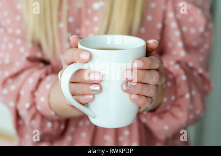 Weibliche Hände halten eine weiße Tasse mit Getränk. Close Up. Unscharfer Hintergrund Stockfoto