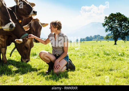 Frau Verklebung mit Kuhherde auf Feld, Sonthofen, Bayern, Deutschland Stockfoto