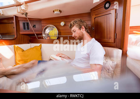 Junger Mann in Segelboot Kabine buchen lesen Stockfoto