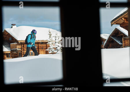 Fenster mit Blick auf männliche Skifahrer zu Fuß durch tiefen Schnee in der Nähe von Hütten, Alpe-d'Huez, Rhône-Alpes, Frankreich Stockfoto