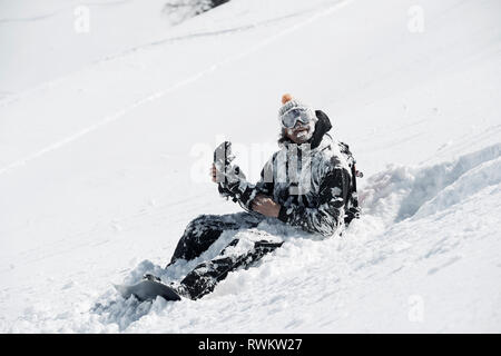 Männliche Snowboarder im Schnee sitzen auf Berghang abgedeckt, Alpe-d'Huez, Rhône-Alpes, Frankreich Stockfoto