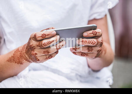 Frau mit Henna Tattoo auf Händen über Smartphone Stockfoto