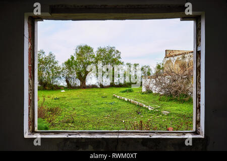 Innenraum eines zerstörten Haus mit einem gebrochenen Fenster anzeigen einer grünen Wiese feld landschaft Stockfoto