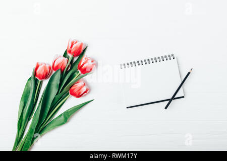 Flach Anordnung der Leere Notepad öffnen und Strauß mit frischen Tulpen Blumen auf weißem Schreibtisch aus Holz, Ansicht von oben. Stockfoto